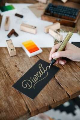 a person writing diwali on black paper